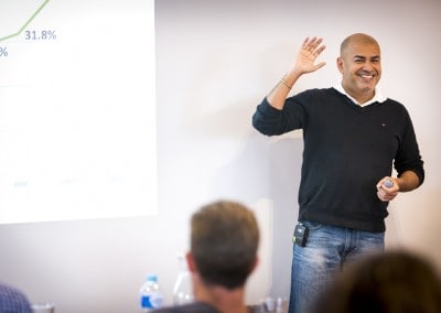 Smiling male speaker waving to audience during a business workshop with growth chart projected on screen