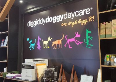 Diggiddy Doggy Daycare reception desk with colourful dog silhouette wall sign and tagline 'coz dogs digg it'